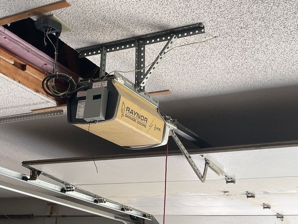 Raynor garage door opener installed on the ceiling with metal support brackets.