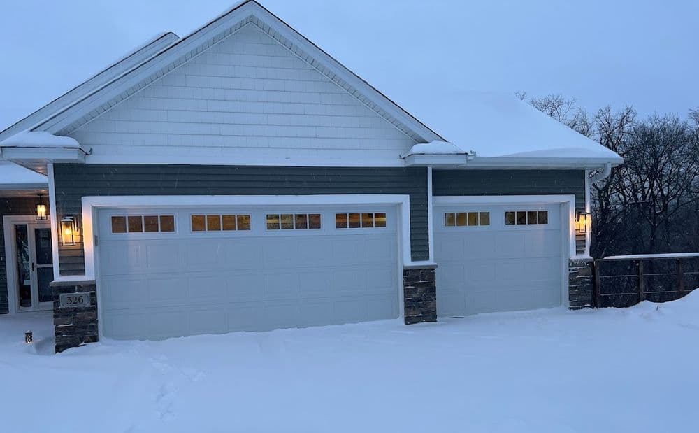 Modern home exterior with snow-covered driveway and two-car garage at dusk.