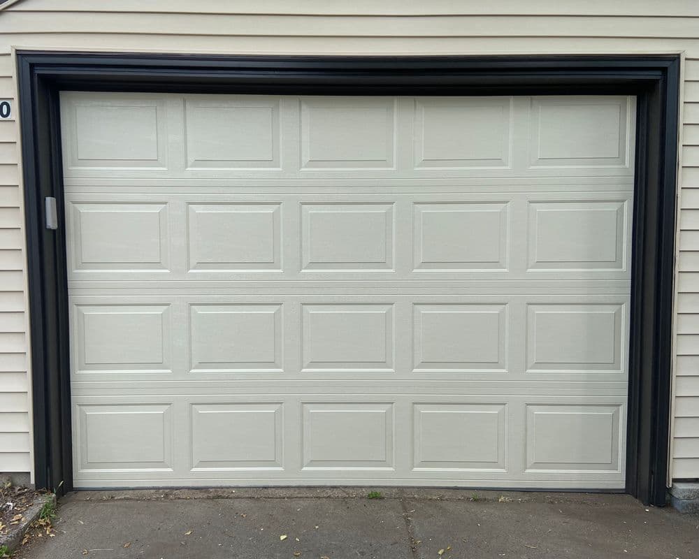 White garage door with raised panels, framed in black, set against a light exterior wall.