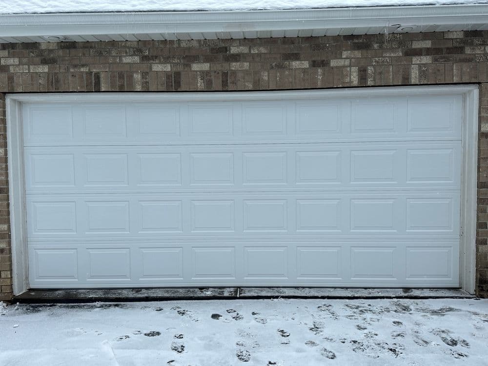 White garage door on a brick wall, snowy ground with paw prints.