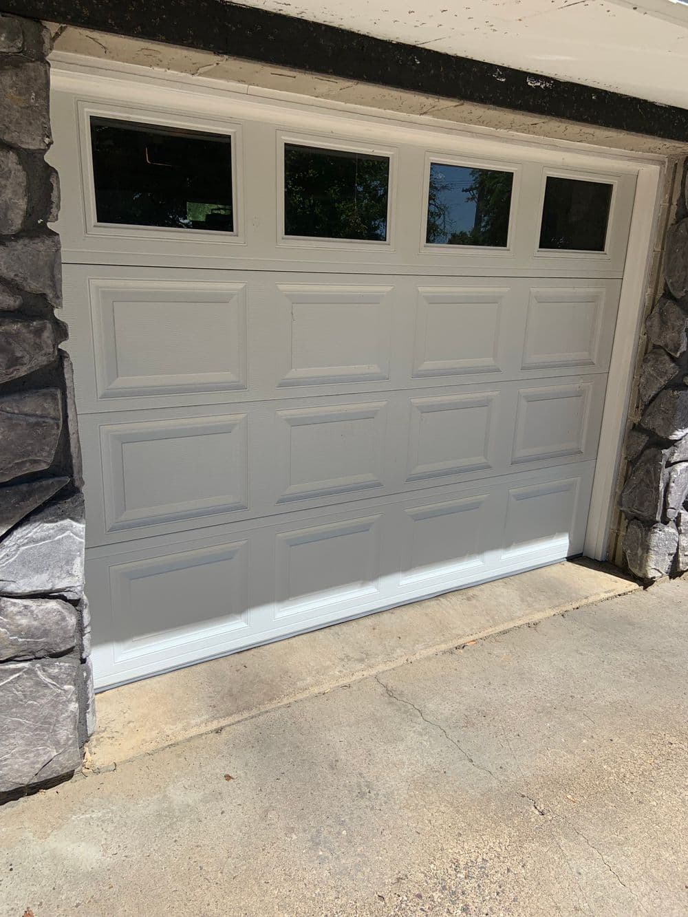 White garage door with decorative windows, framed by stone exterior.