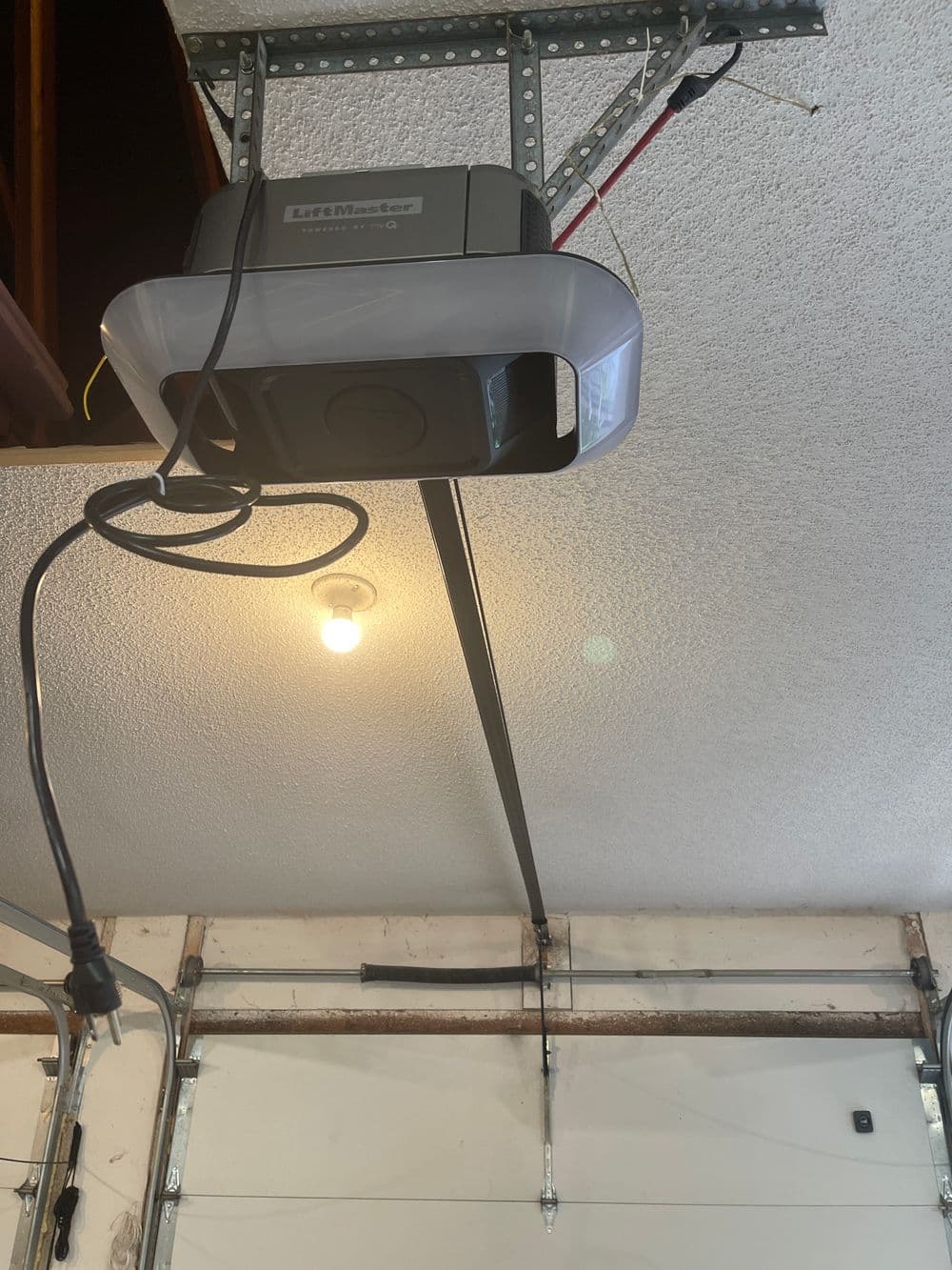 Garage door opener mounted on ceiling with illuminated light, cables visible in the background.