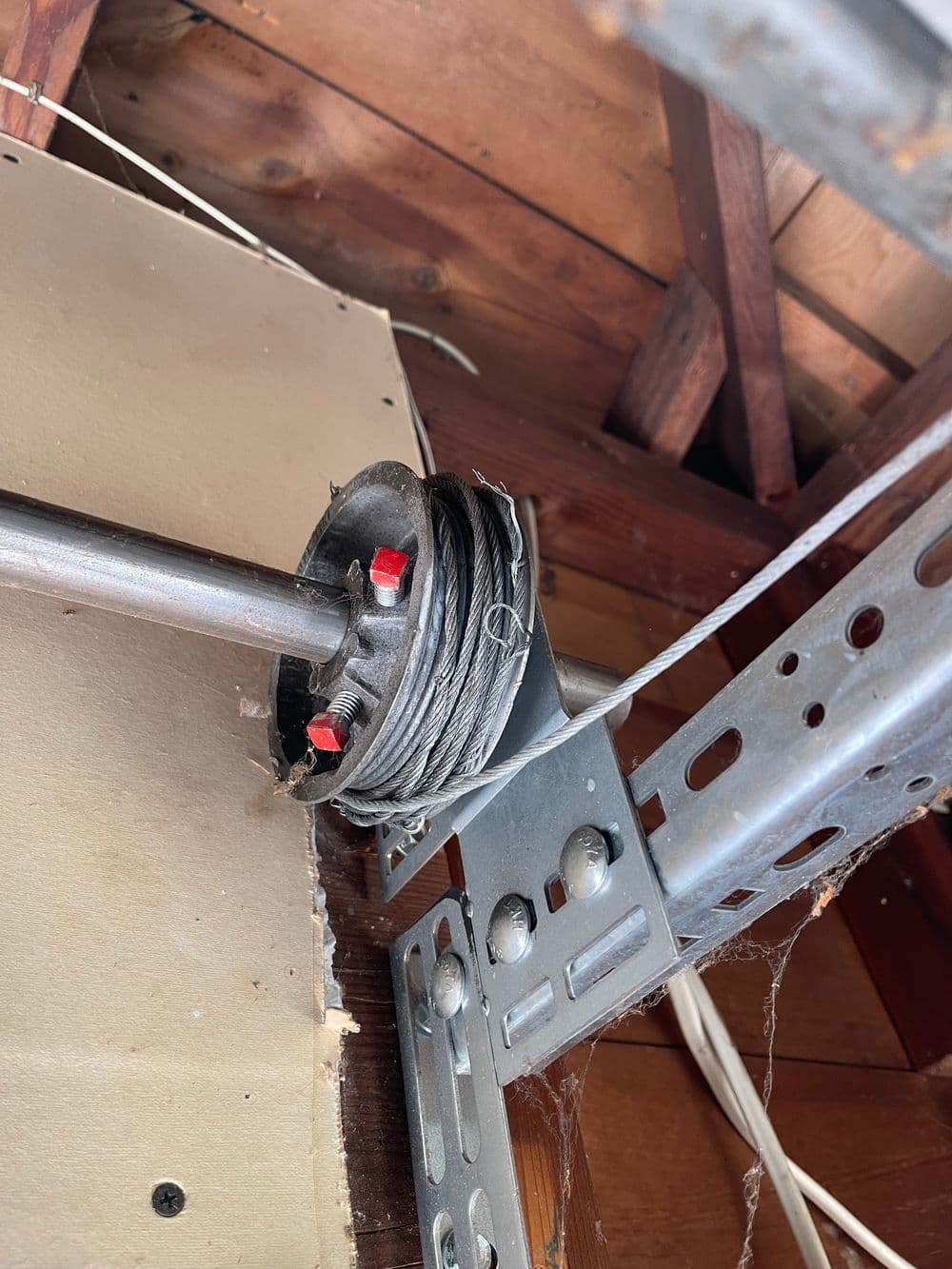 Garage door tension spring mechanism with steel wire and mounting hardware inside a wooden structure.