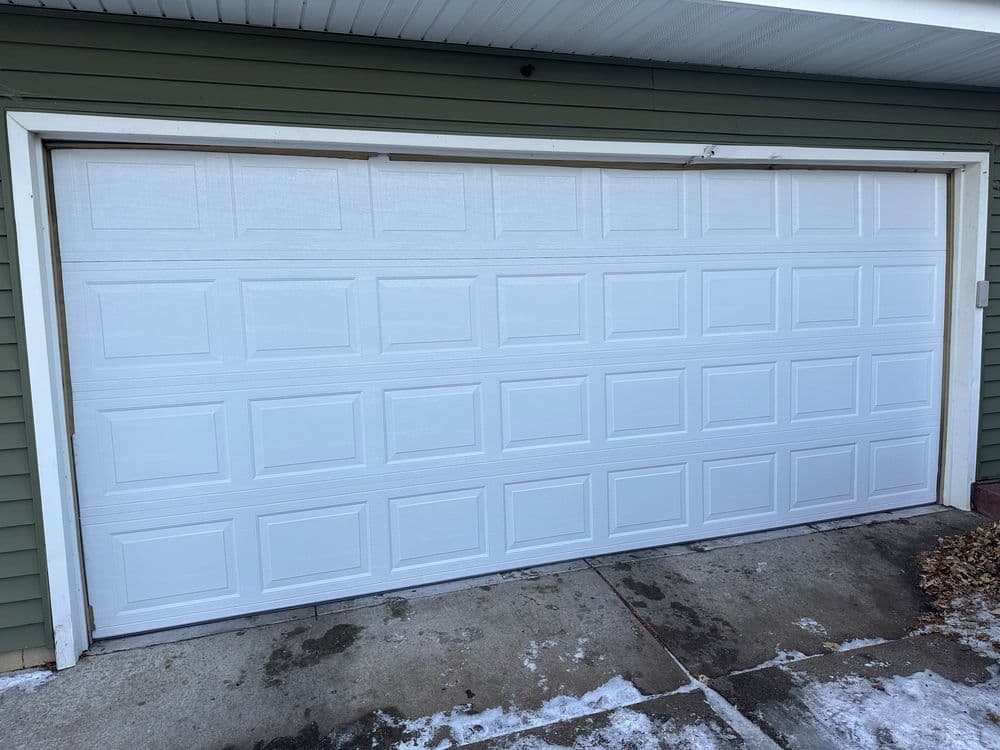 White garage door on a green house exterior with snow on the ground.