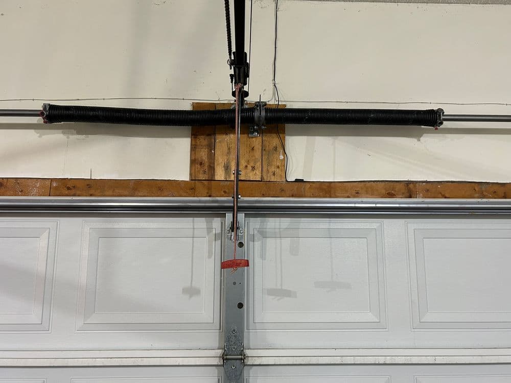 Garage door spring and tension cable system mounted on the wall, above a closed garage door.