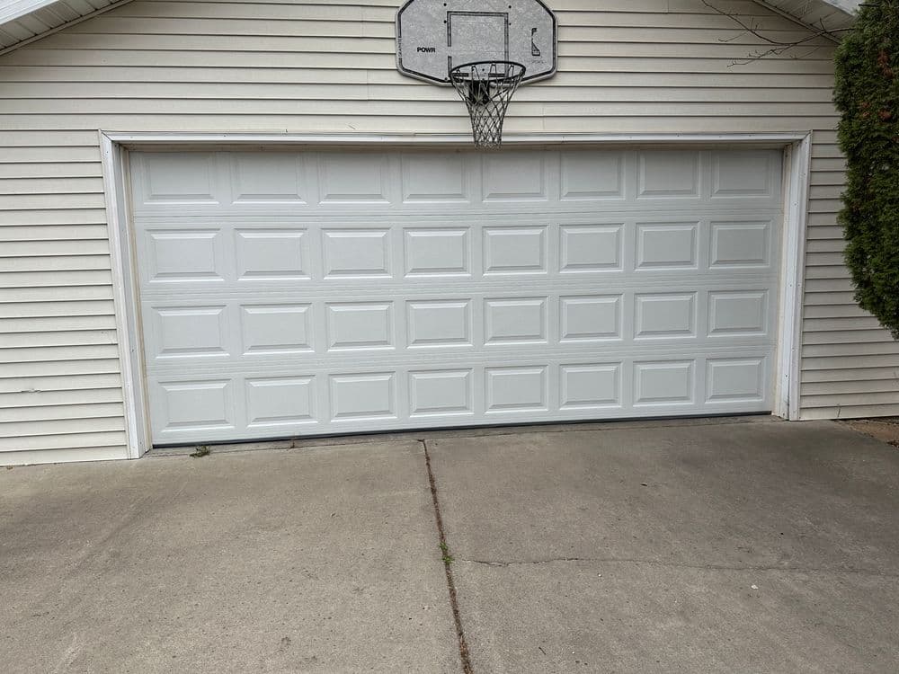 White garage door with panel design and basketball hoop above, set against a house exterior.