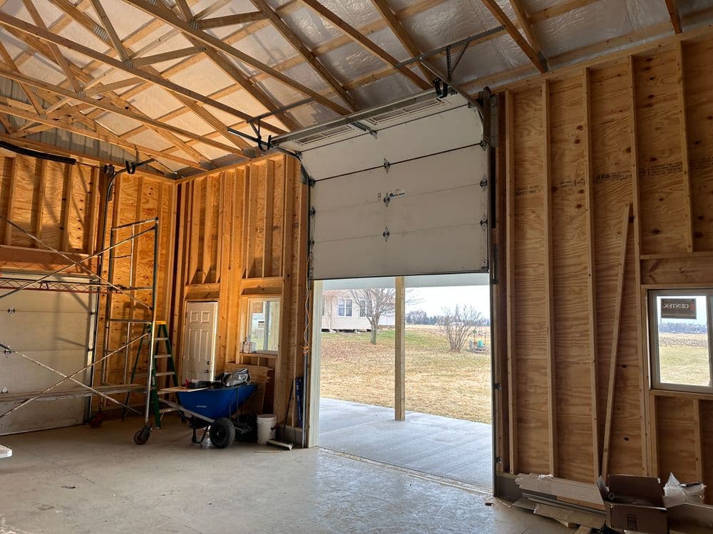 Interior of a garage with a large door open, showcasing wooden framing and tools.
