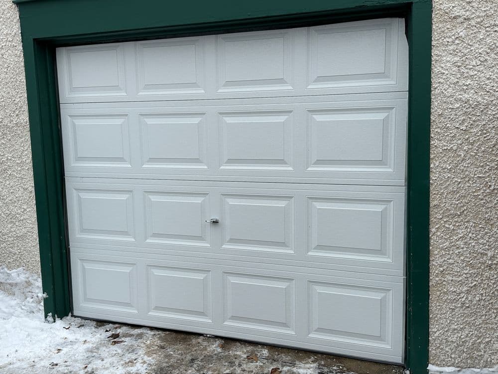 White garage door with geometric panel design, framed by green trim on a snowy surface.