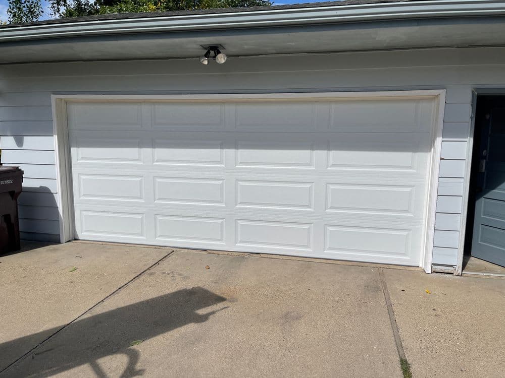 White garage door on a residence with a blue exterior and concrete driveway.