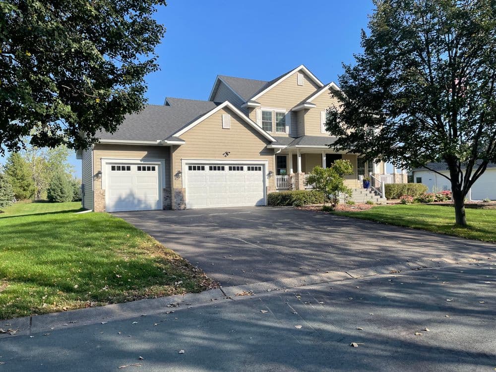 Elegant two-story house with a spacious driveway and lush green landscaping on a sunny day.