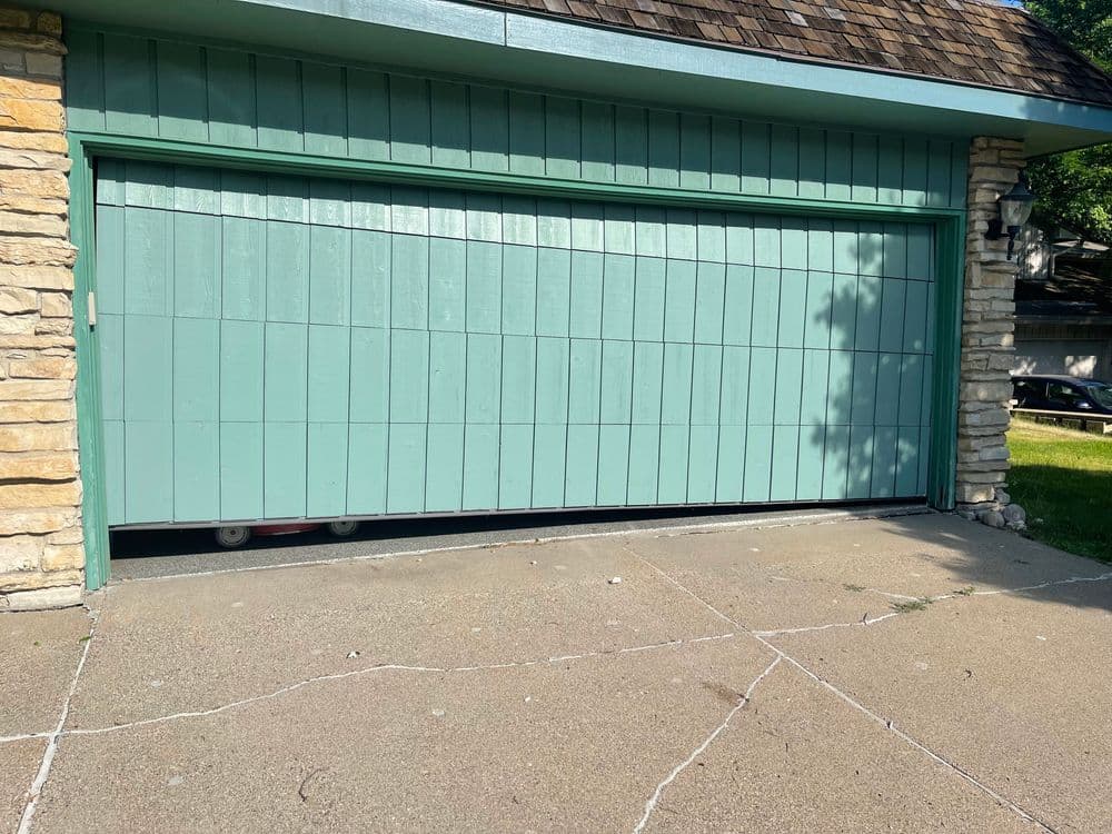 teal garage door with stone accents and driveway on a sunny day