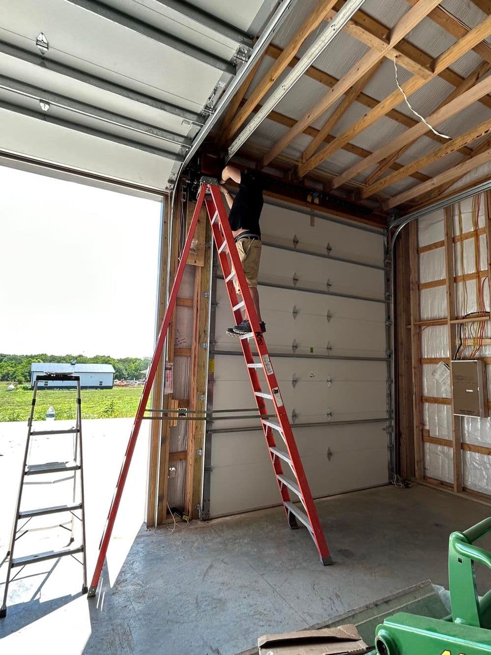 Person on a ladder inside a garage, adjusting overhead fixtures in a sunny environment.
