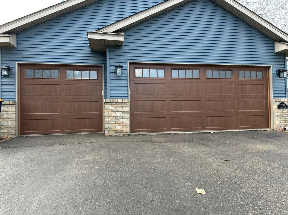 Modern blue house with two large brown garage doors and stone accents.