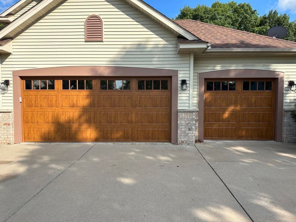 Two wooden garage doors with glass panels, framed in brown, on a suburban home's exterior.