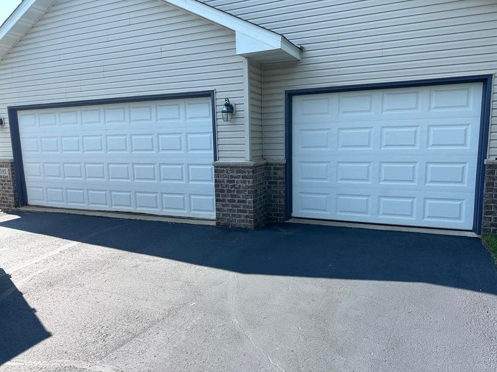 Two white garage doors with brick accents on a suburban home exterior.