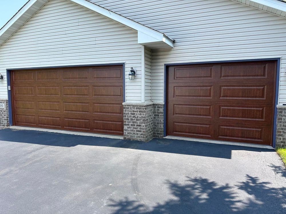 Two wooden garage doors on a suburban home with a light-colored siding exterior.